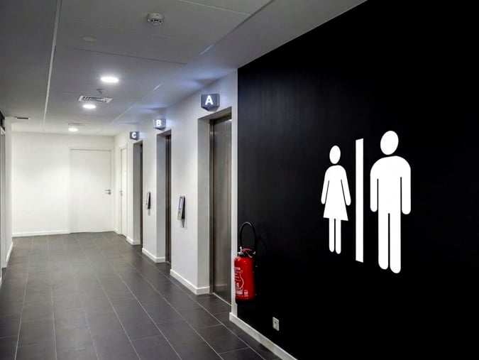 Signalétique sanitaire directionnelle avec pictogrammes WC homme femme sur mur noir, couloir de bureaux