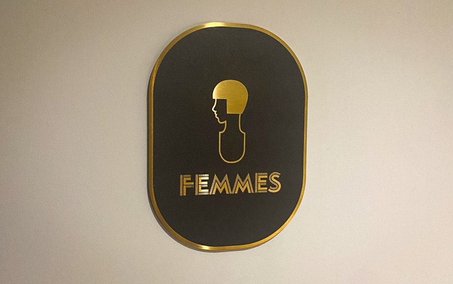 signalétique directionnelle d'hôtel présentant une plaque Femmes en inox or brossé avec pictogramme de profil, style Art déco